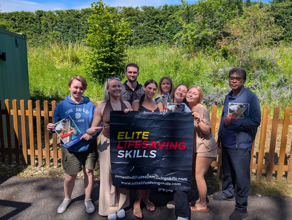 Group of people holding a "Elite Lifesaving Skills" banner in a lush outdoor setting.